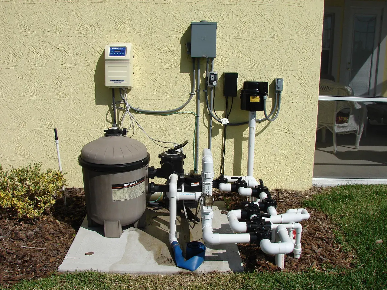 Outdoor pool pump and filtration system installed beside a house.
