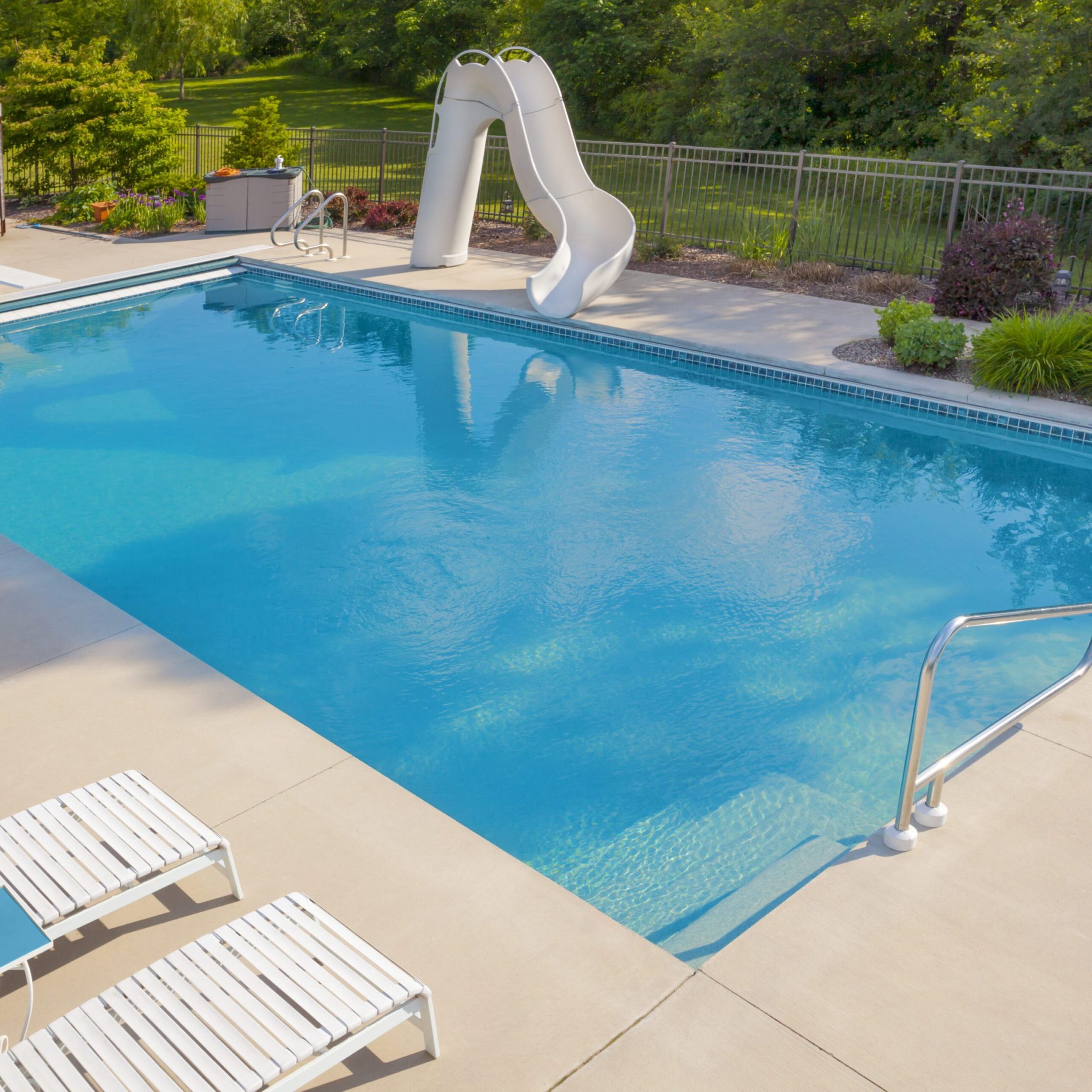 A clear blue swimming pool with a white slide.